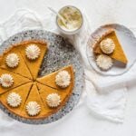 A fresh baked pumpkin pie, sliced and topped with whipped cream and pumpkin pie spice.