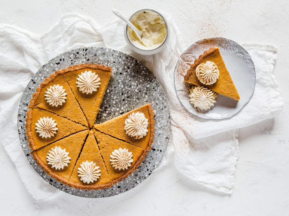 Overhead shot of Keto Pumpkin Pie with a plate with a single slice next to it. Both are topped with fresh whipped cream.