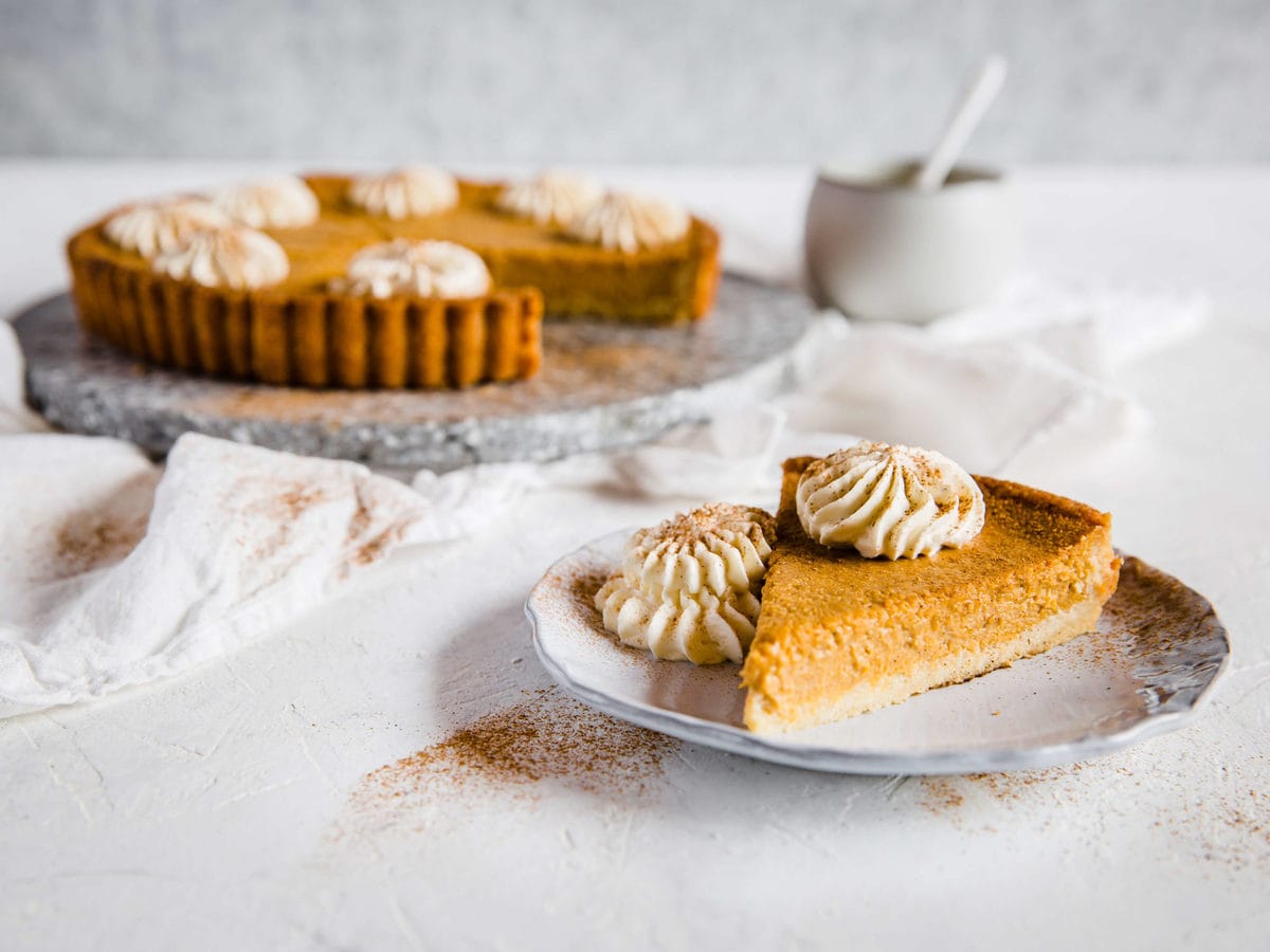 Keto Pumpkin Pie with a plate with a single slice next to it. Both are topped with fresh whipped cream.