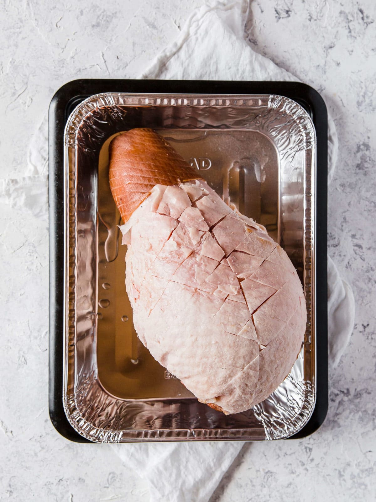 a full ham, scored on top, in an aluminum baking tray, ready to go into the oven