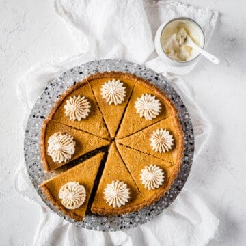 an overhead shot of a pumpkin pie, sliced and topped with fresh whipped cream.