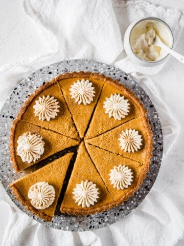 an overhead shot of a pumpkin pie, sliced and topped with fresh whipped cream.