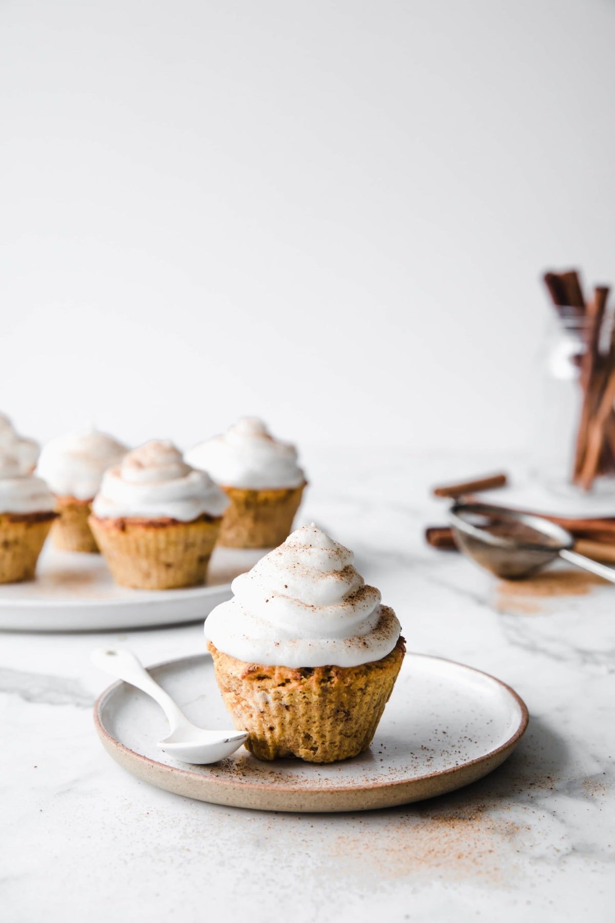 low carb pumpkin spice cupcakes, frosted with marshmallow frosting, served on a porcelain plate, with a spoon