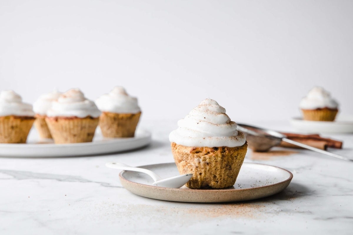 low carb pumpkin spice cupcakes, frosted with marshmallow frosting, served on a porcelain plate, with a spoon