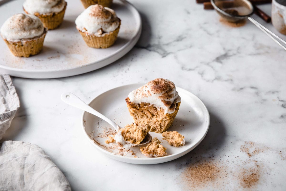 low carb pumpkin spice cupcakes, frosted with marshmallow frosting, served on a porcelain plate, with a spoon