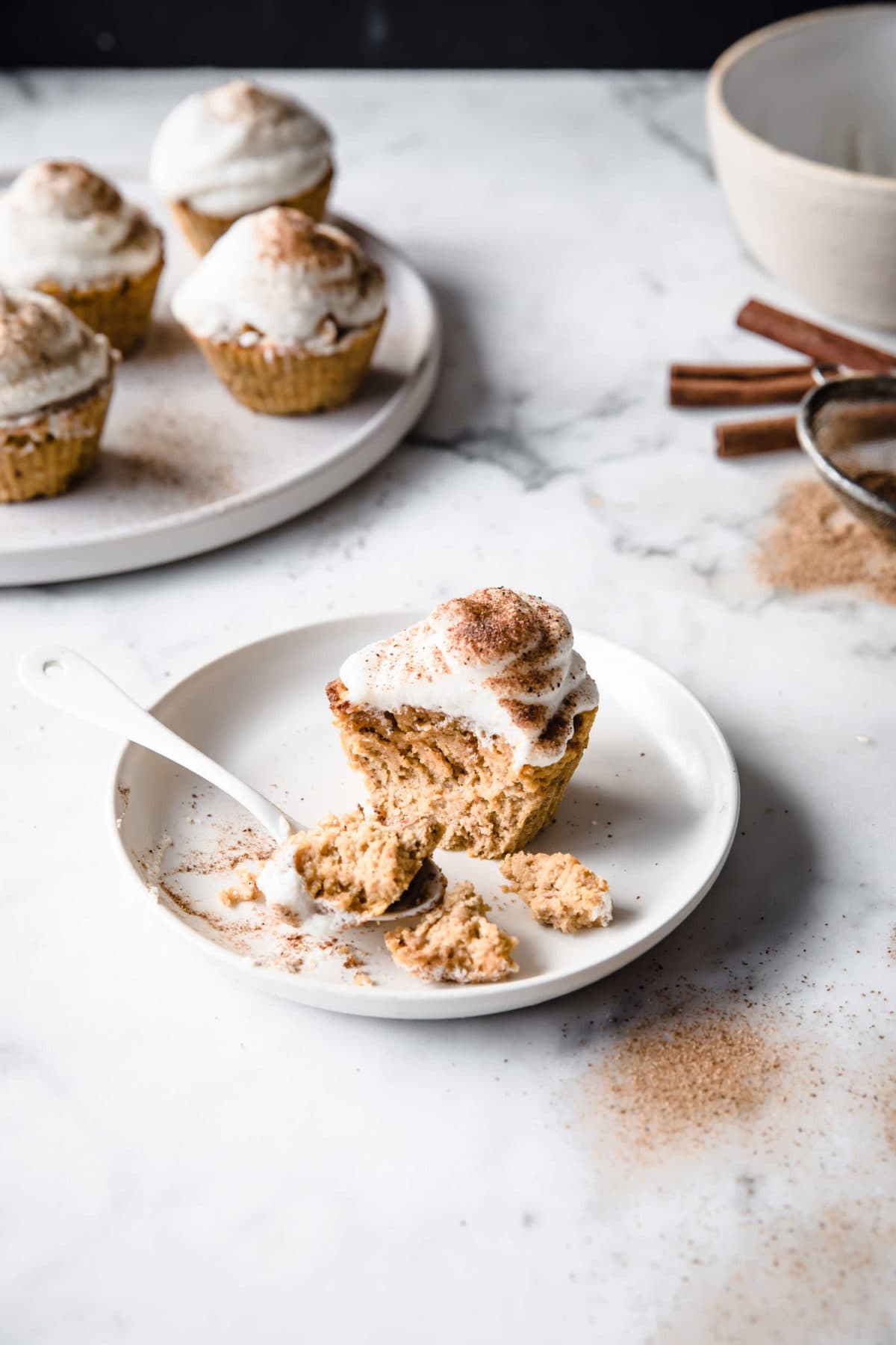 low carb pumpkin spice cupcakes, frosted with marshmallow frosting, served on a porcelain plate, with a spoon