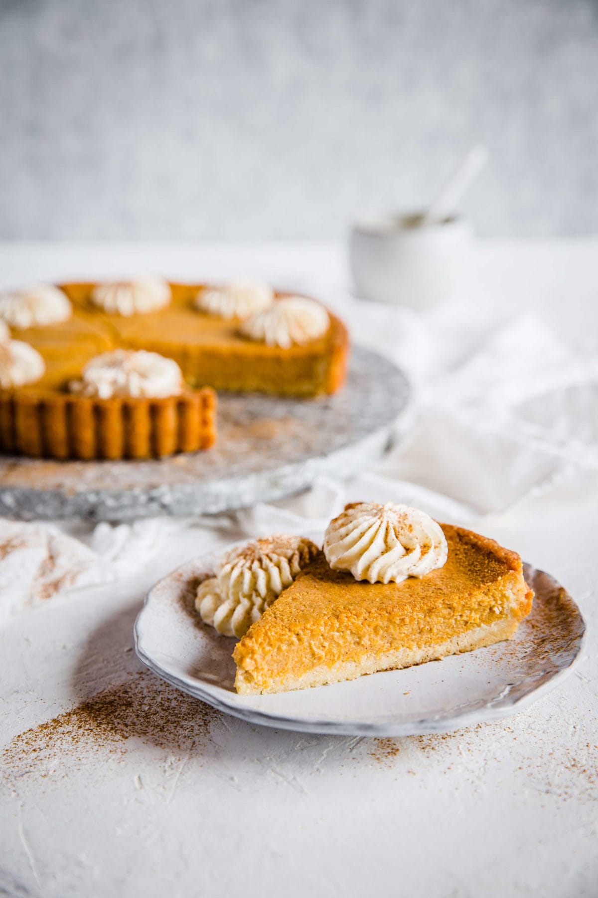 a slice of pumpkin pie on a plate, garnished with fresh whipped cream and cinnamon.