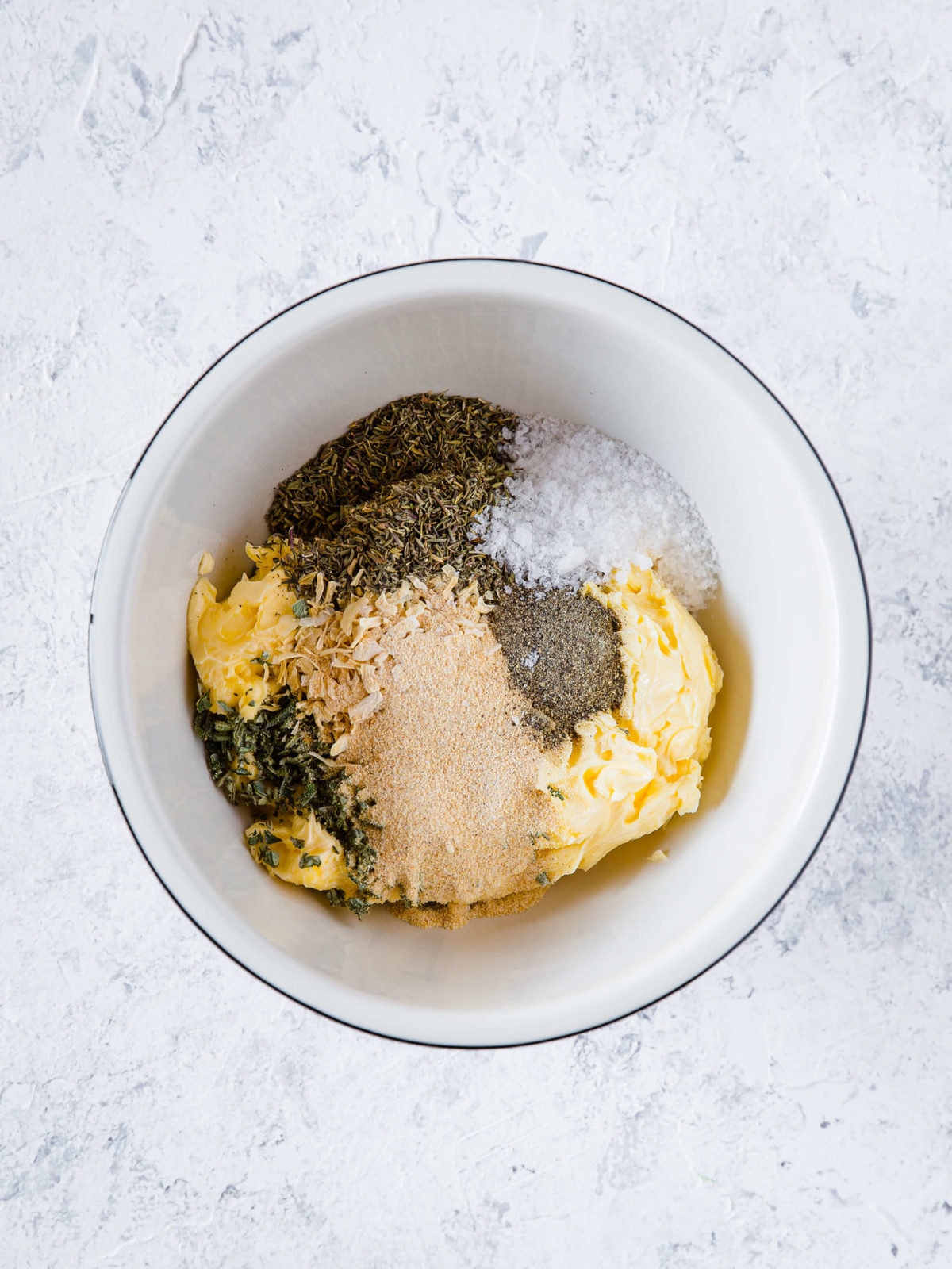 A small mixing bowl with butter, thyme, sage, minced onion, salt, and pepper. 