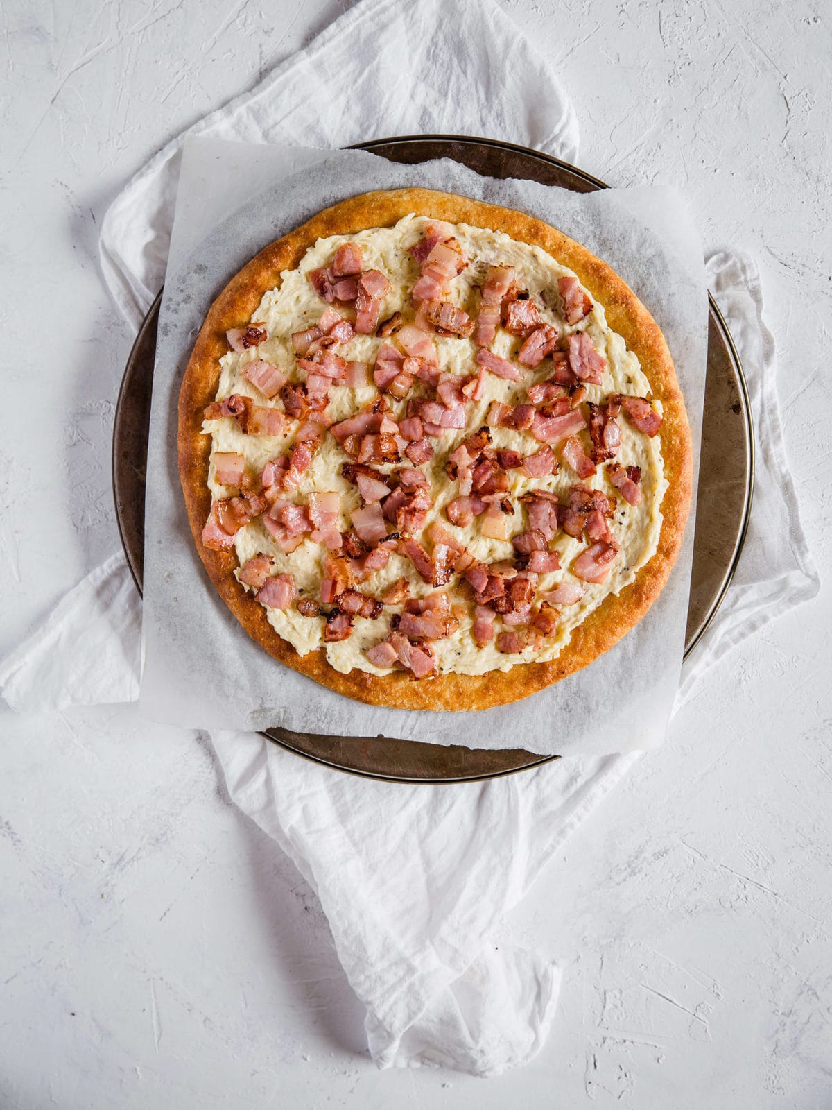 overhead shot of a low carb pizza crust, topped with cream sauce and bacon