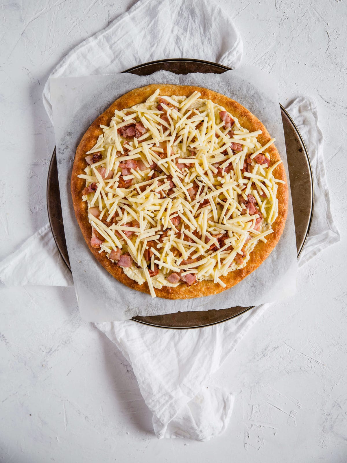 overhead shot of a low carb pizza crust, topped with cream sauce and bacon, and cheese
