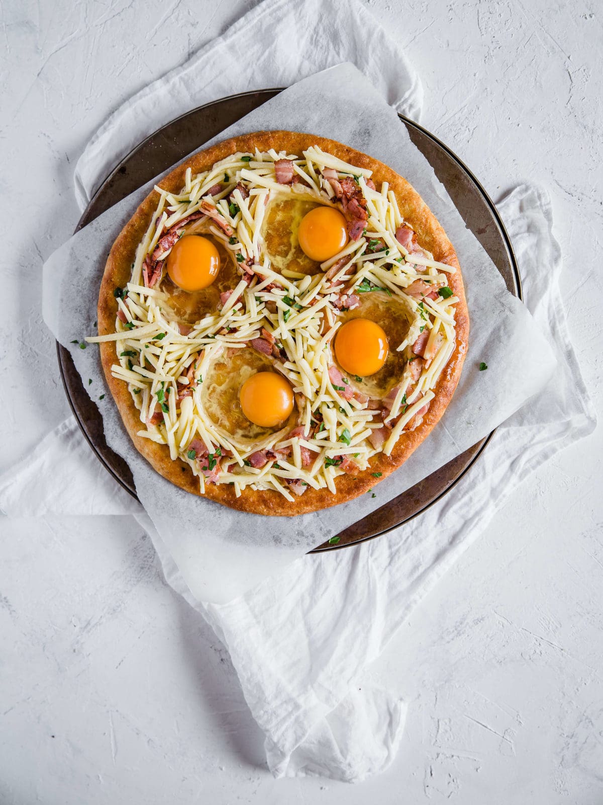 overhead shot of a low carb pizza crust, topped with cream sauce and bacon, cheese, and eggs