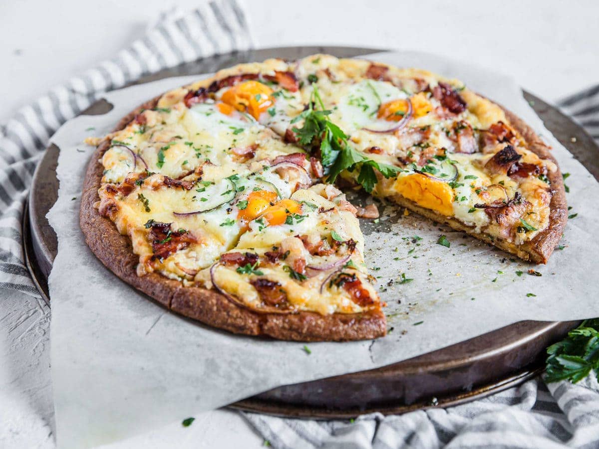 overhead shot of a low carb pizza crust, topped with cream sauce and bacon, cheese, and eggs