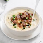 white bowl full of creamy chicken soup, topped with crispy bacon, cheese, and jalapeño.