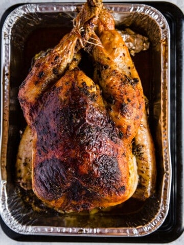 An aluminum pan with a butter basted turkey, fresh out of the oven.