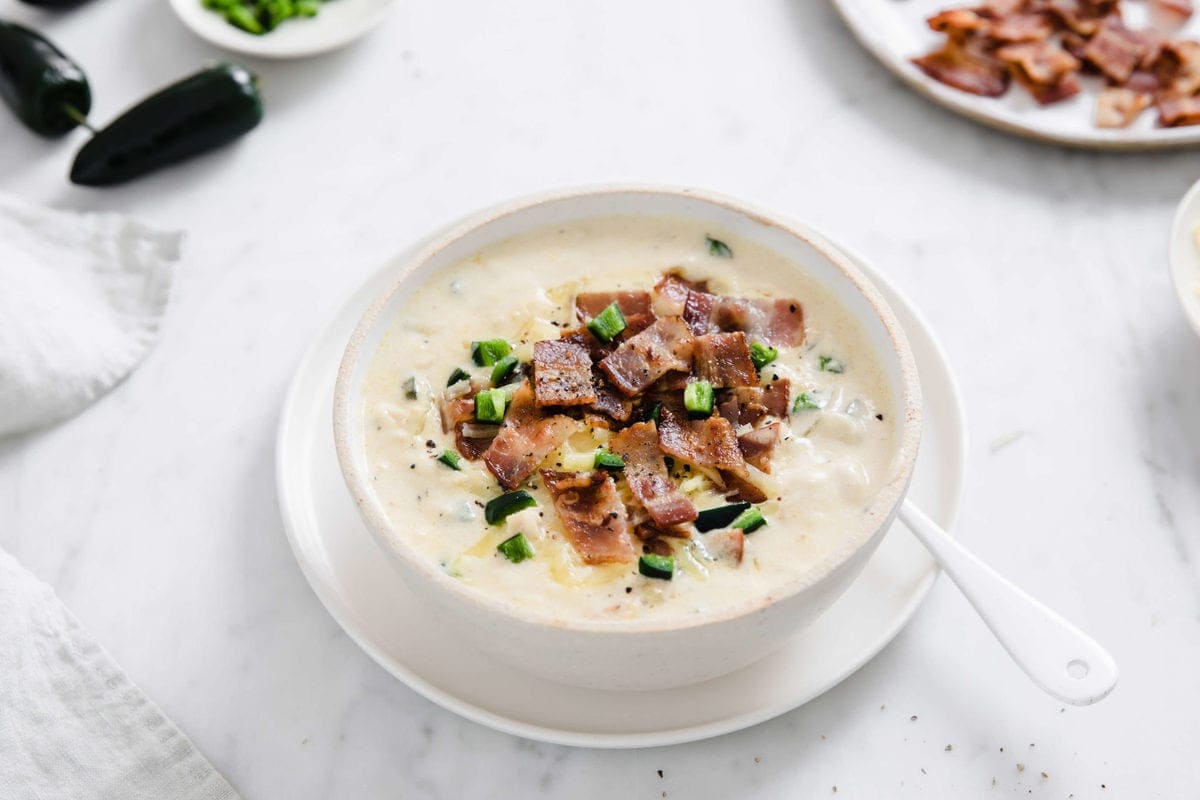 white bowl full of creamy chicken soup, topped with crispy bacon, cheese, and jalapeño