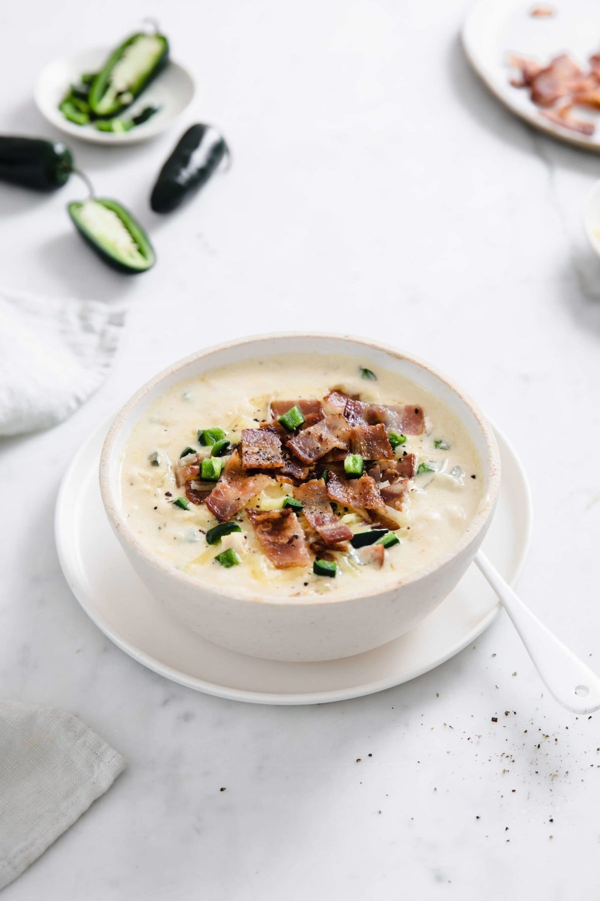 white bowl full of creamy chicken soup, topped with crispy bacon, cheese, and jalapeño