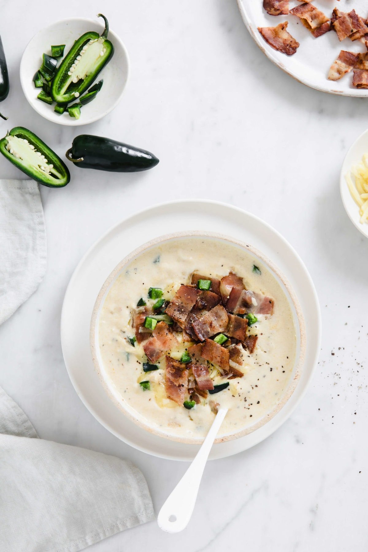 white bowl full of creamy chicken soup, topped with crispy bacon, cheese, and jalapeño.
