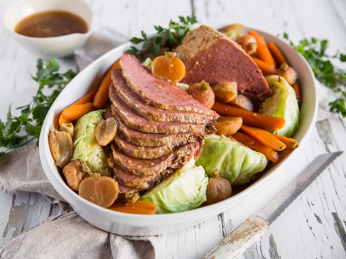 A casserole dish with sliced corned beef, cabbage, carrots, radishes and parsley.