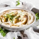 A bowl of creamy cauliflower mash with keto pan gravy and fresh herbs as a garnish.