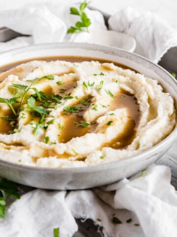 A bowl of creamy cauliflower mash with keto pan gravy and fresh herbs as a garnish.