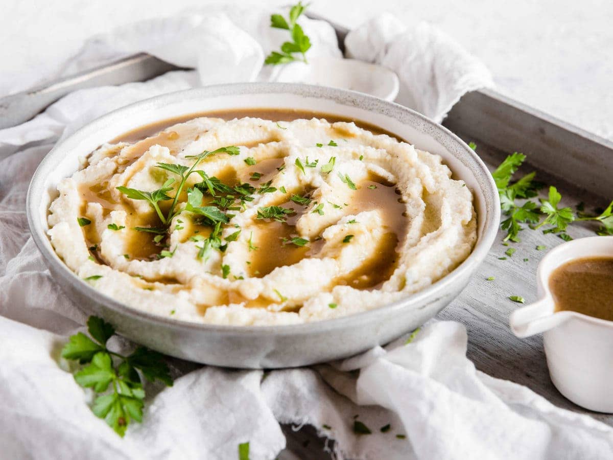 A bowl of creamy cauliflower mash with keto pan gravy and fresh herbs as a garnish.