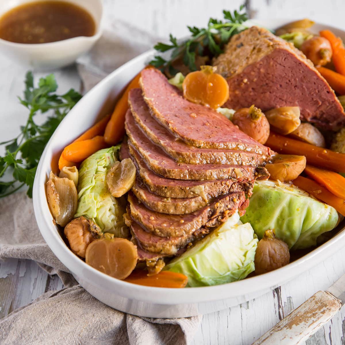 A casserole dish with sliced corned beef, cabbage, carrots, radishes and parsley.