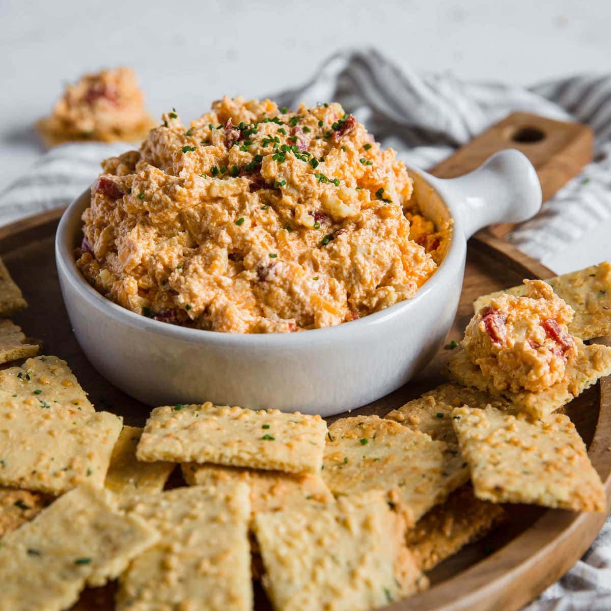 Pimento Cheese Dip, sitting on a wooden charcuterie board piled with Parmesan Chive and Garlic Keto Crackers.