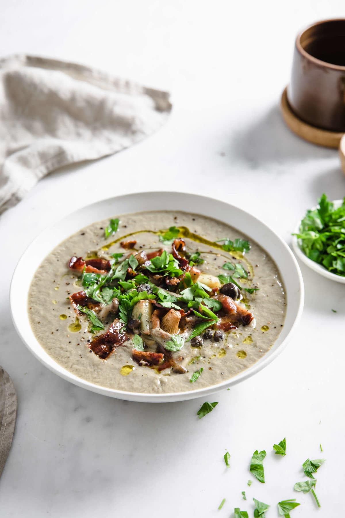 Bowl of mushroom soup on a white background, garnished with mushrooms, garlic, bacon and parsley