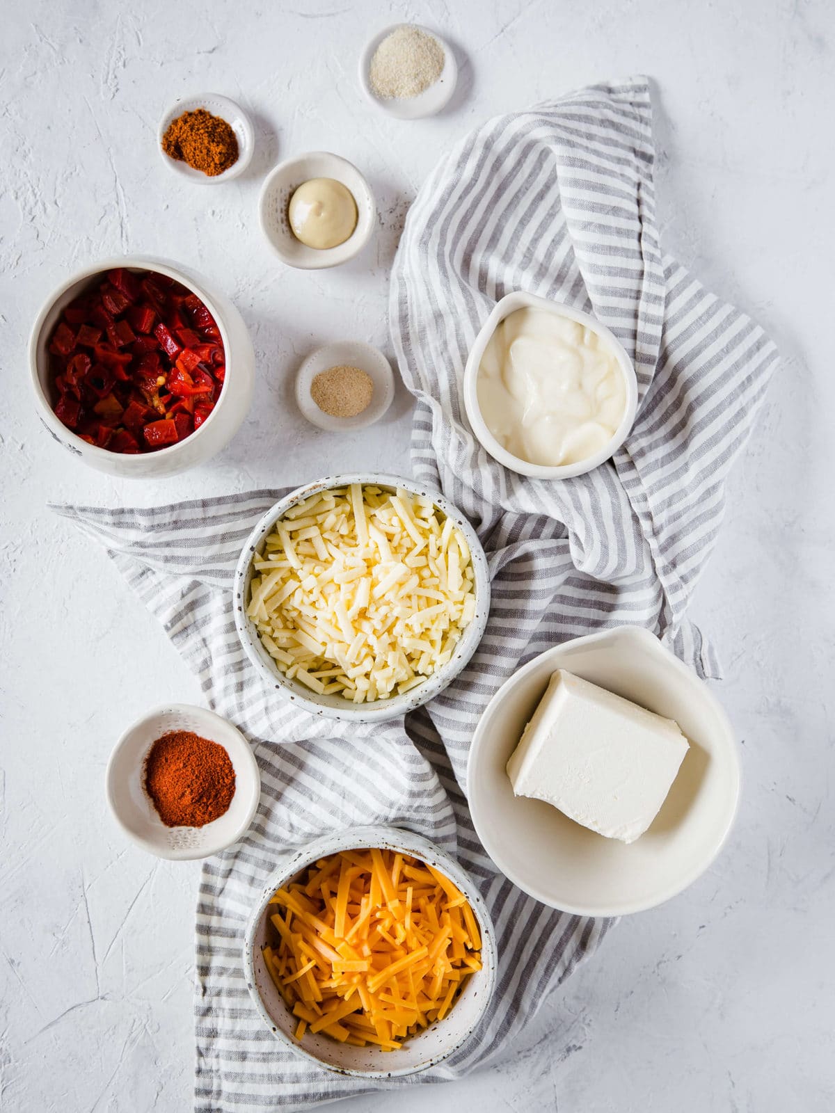 All of the ingredients to make Pimento Cheese Dip: shredded cheddar, shredded sharp cheddar, cream cheese, mayonnaise, cayenne, paprika, garlic powder, onion powder, Dijon mustard, and chopped pimento peppers.