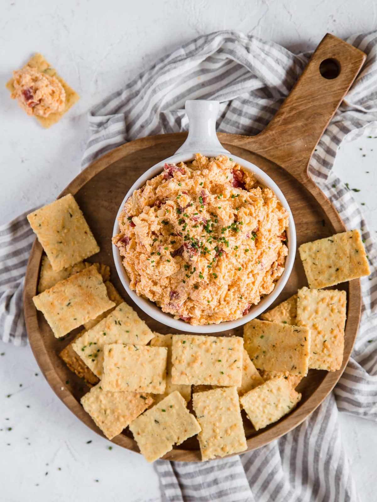 An overhead shot of a cheese dip dish overflowing with Pimento Cheese Dip, sitting on a wooden charcuterie board piled with Parmesan Chive and Garlic Keto Crackers.