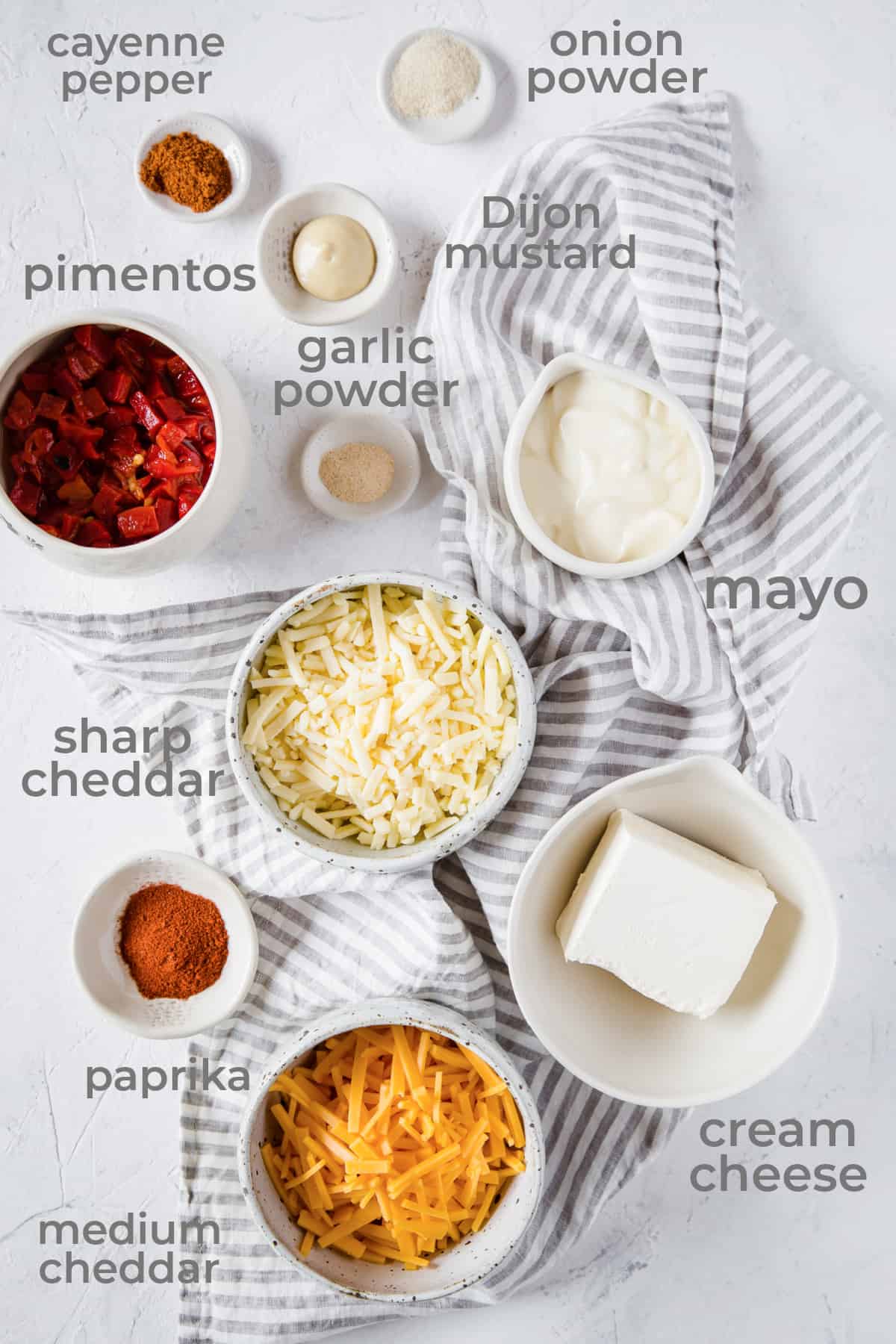 All of the ingredients to make Pimento Cheese Dip: shredded cheddar, shredded sharp cheddar, cream cheese, mayonnaise, cayenne, paprika, garlic powder, onion powder, Dijon mustard, and chopped pimento peppers.