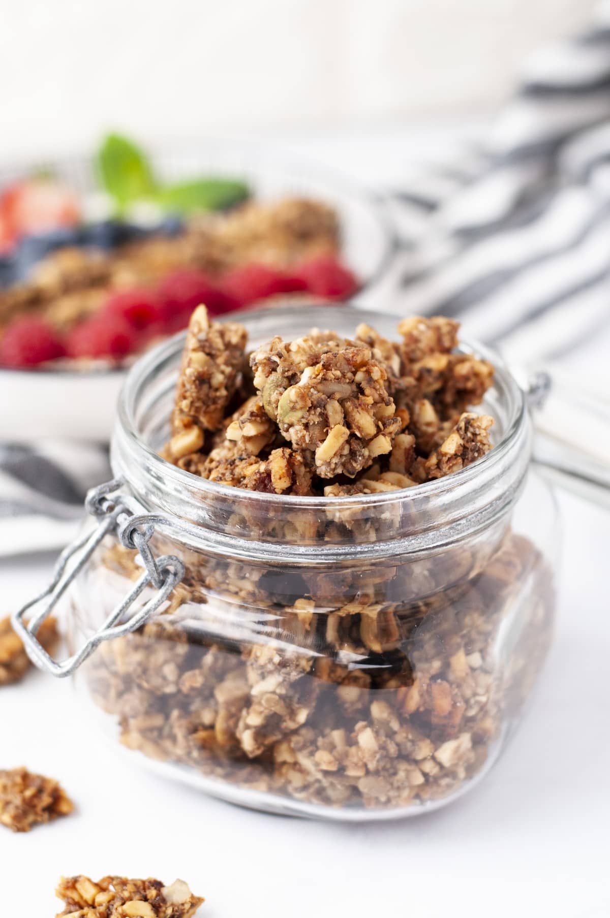 a jar of keto granola with a yogurt parfait blurred in the background