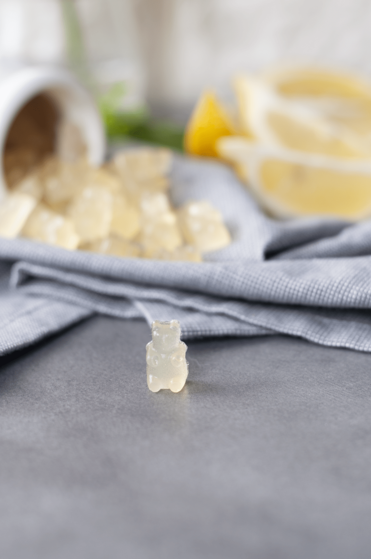 A single lemon gummy bear in the foreground with a pile of gummy bears blurred in the background.