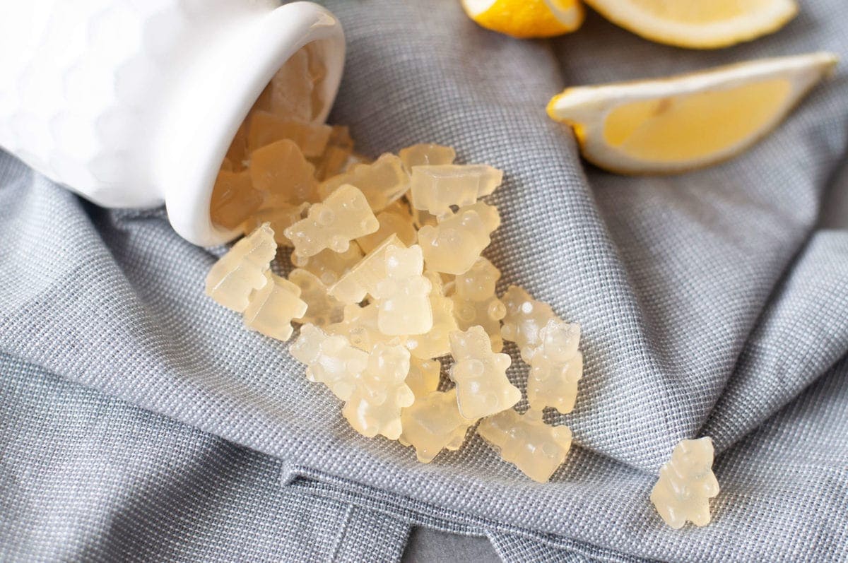 An overhead shot of a white bottle laying on its side, spilling out a bunch of low carb sour lemon gummy bears