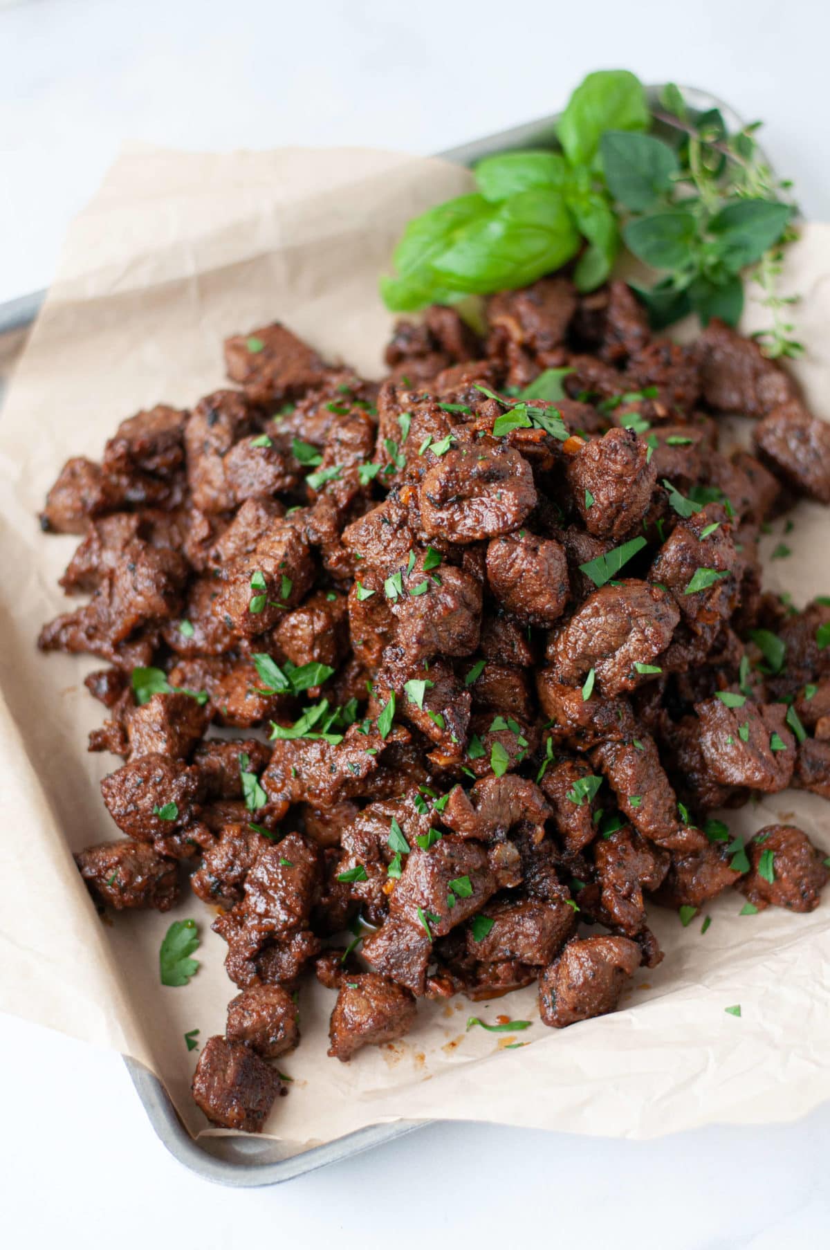 steak bite appetizer served on a baking sheet with parchment paper. garnished with lots of green herbs