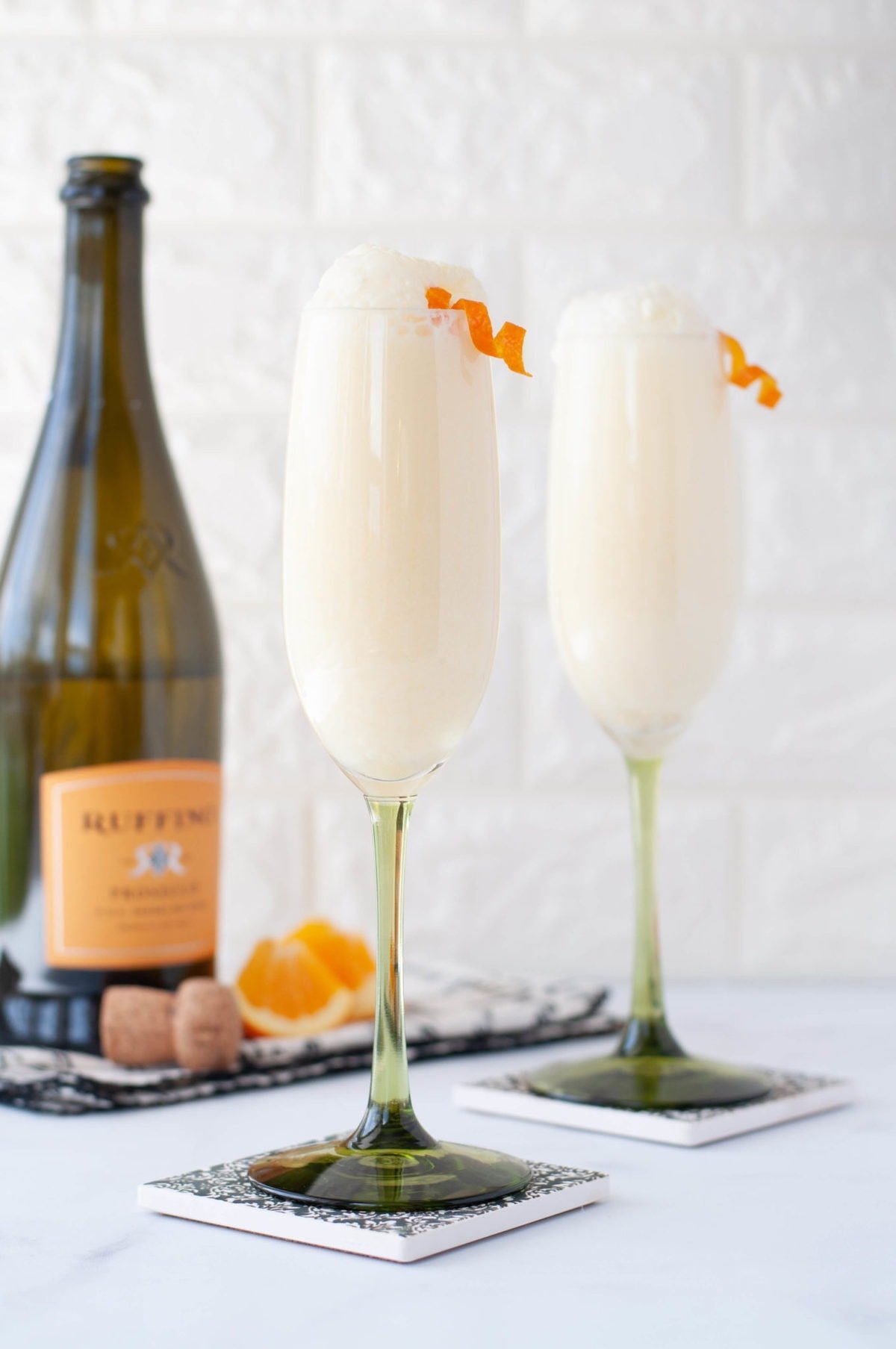 2 champagne flutes in the foreground, with a bottle of champagne in the background