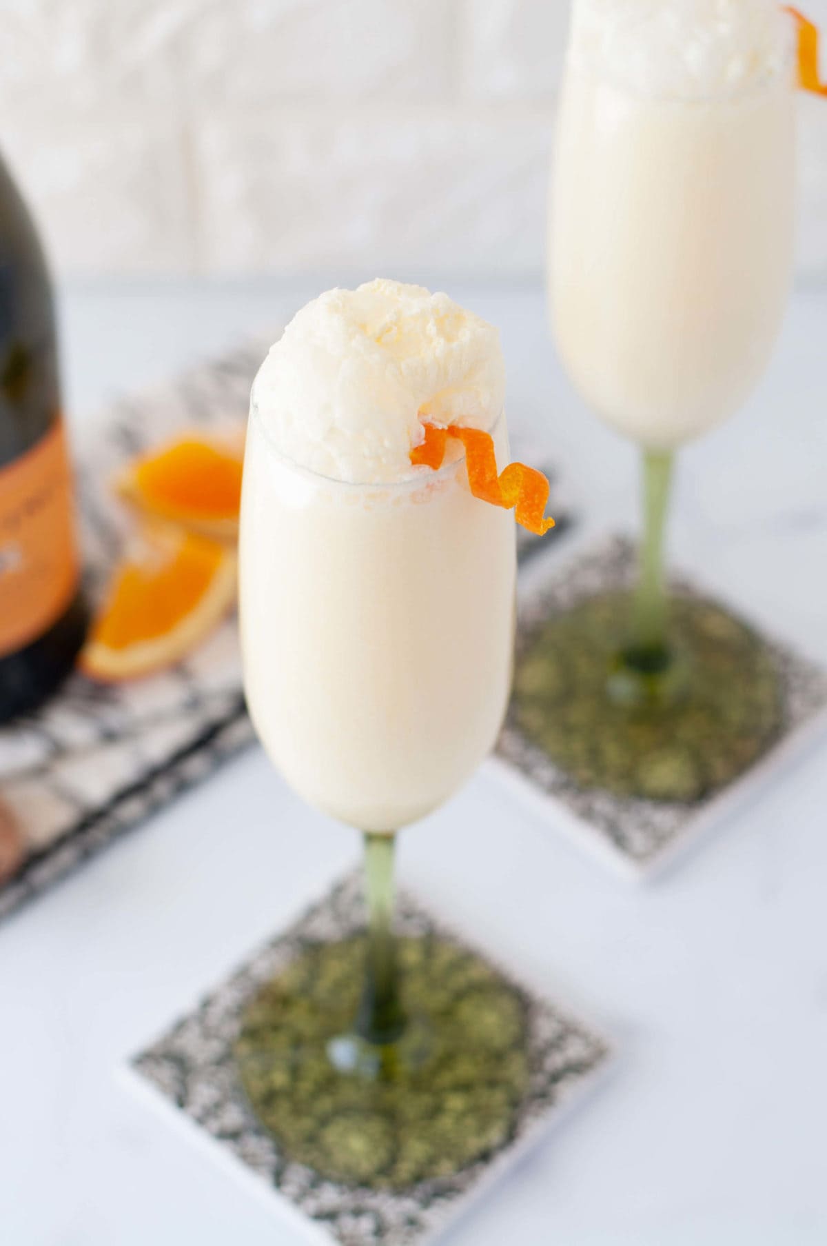 a close up shot of a frothy creamsicle mimosa with an orange twist