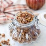 Gluten Free Pumpkin Spice granola in a decorative glass jar, shaped like a pumpikin