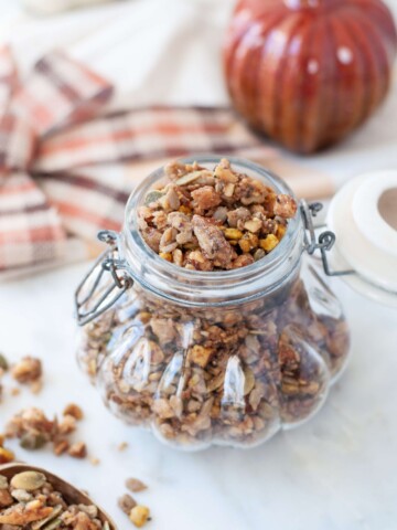 Gluten Free Pumpkin Spice granola in a decorative glass jar, shaped like a pumpikin