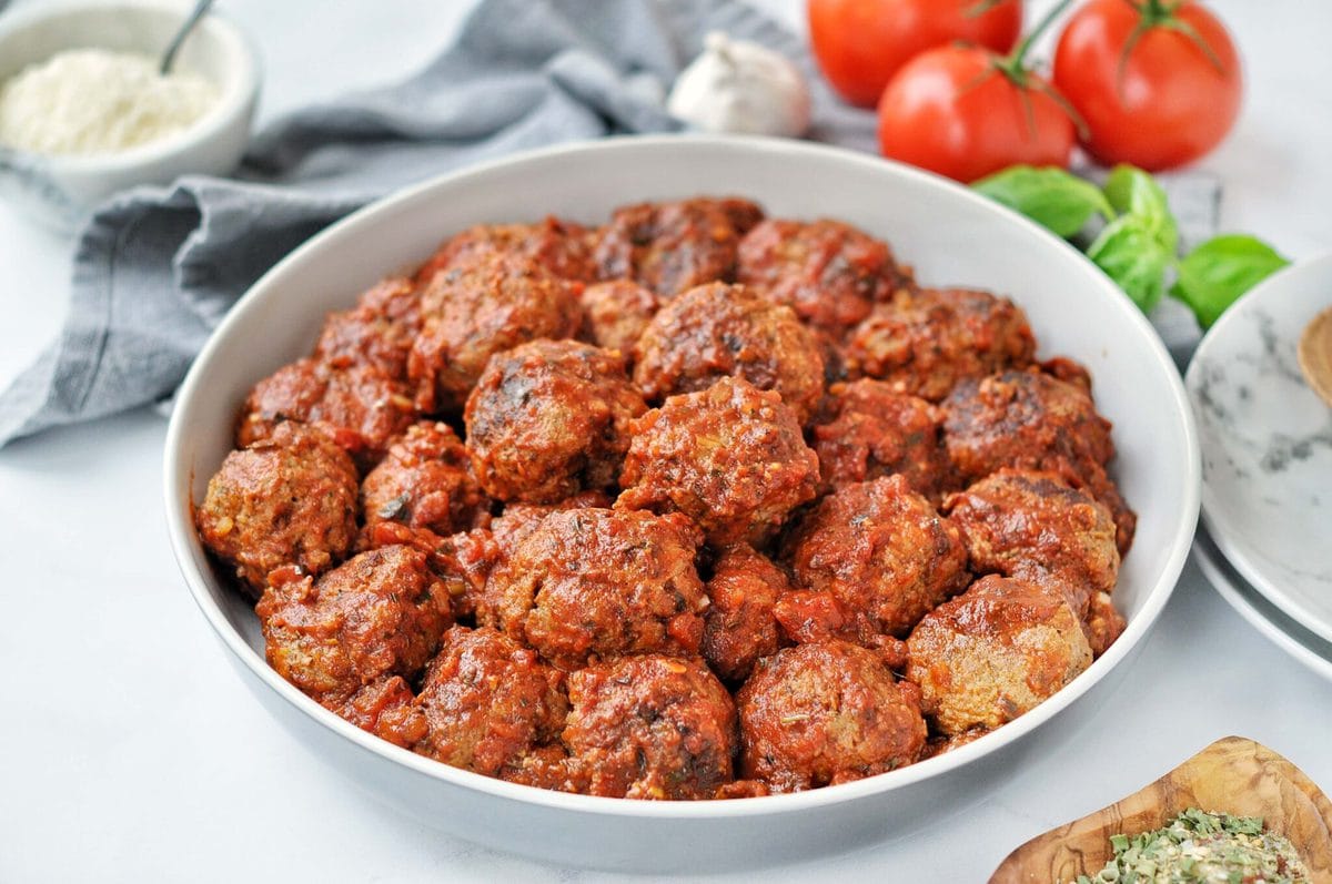 Overhead shot of slow cooked meatballs in tomato sauce. surrounded by fresh ingredients