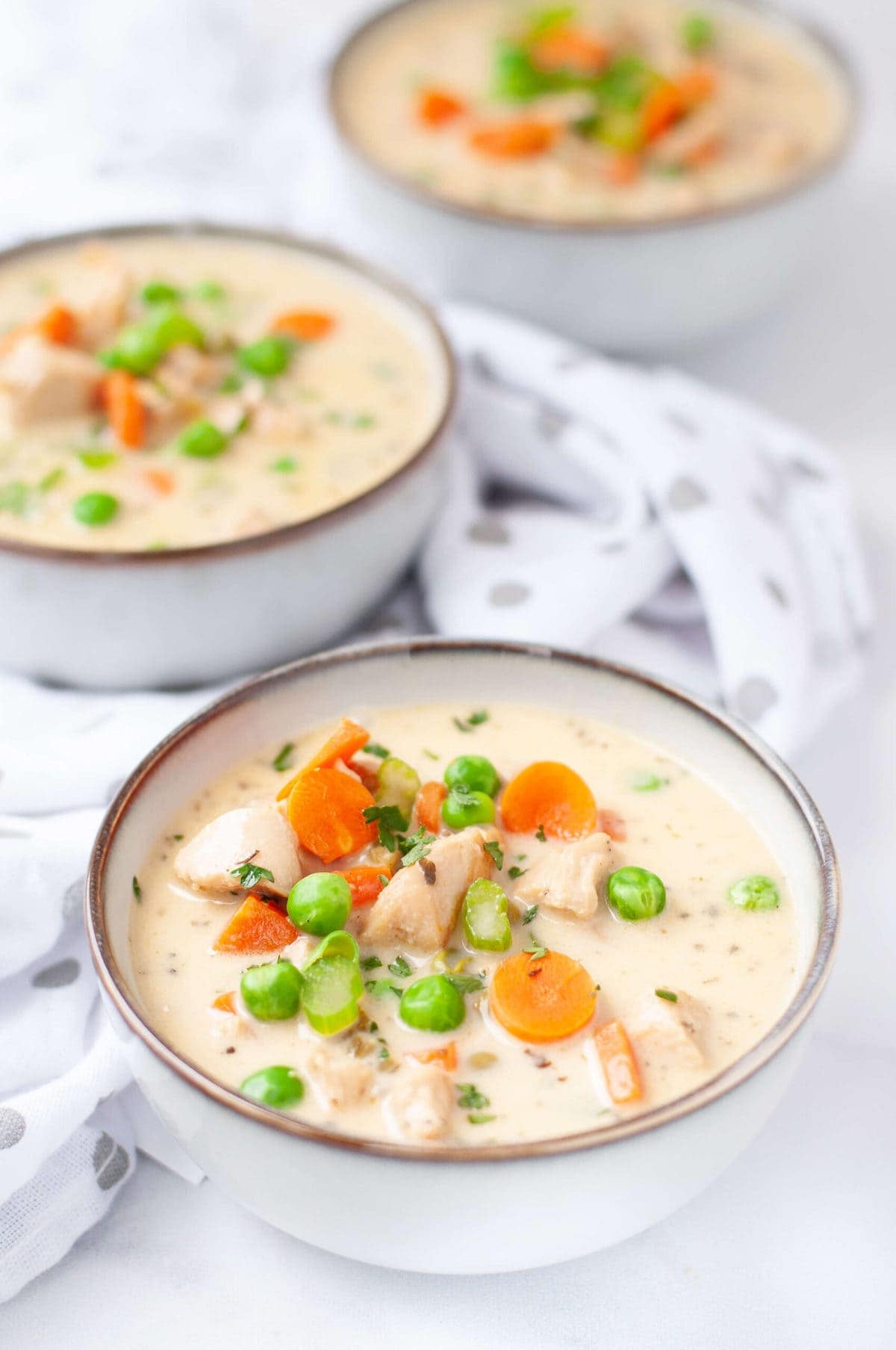 3 bowl of chicken pot pie soup garnished with carrots, peas and celery 