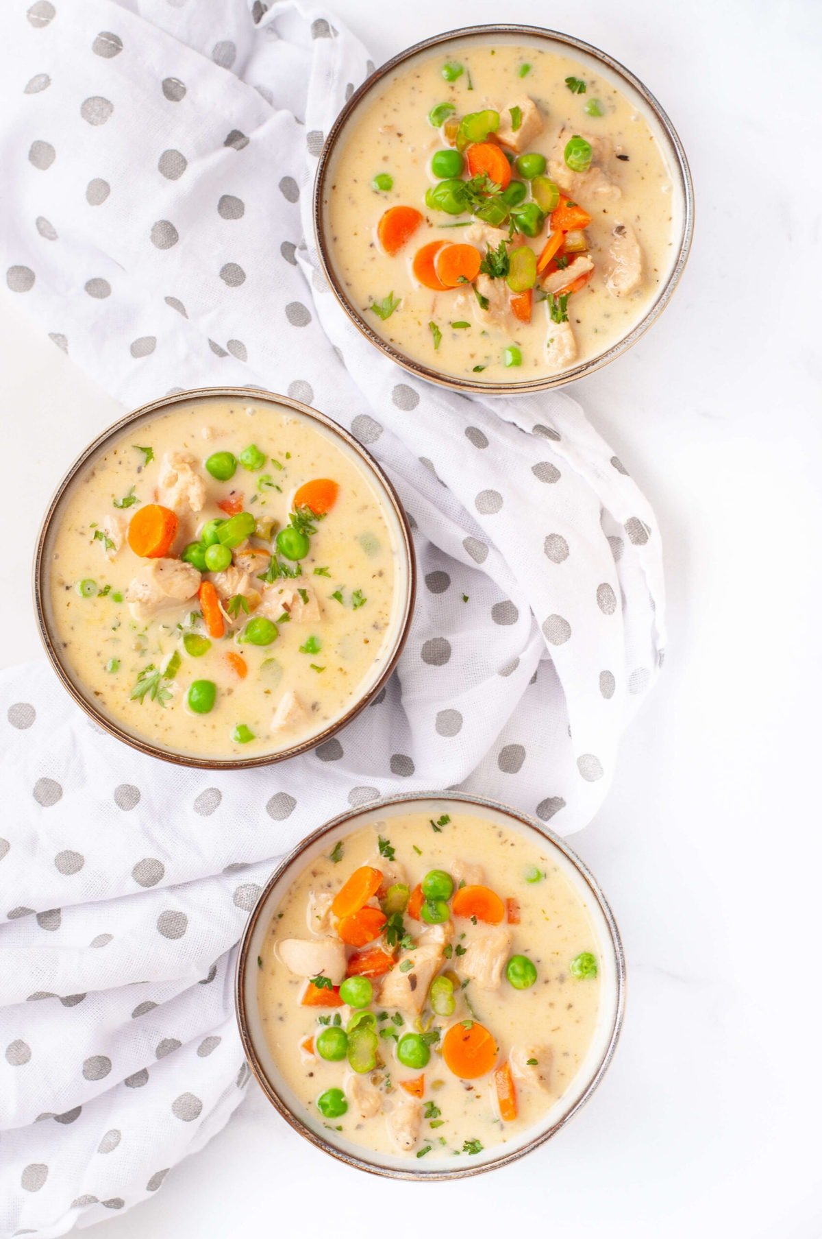 overhead shoot of 3 bowls of creamy chicken pot pie soup topped with carrots, celery, and peas.