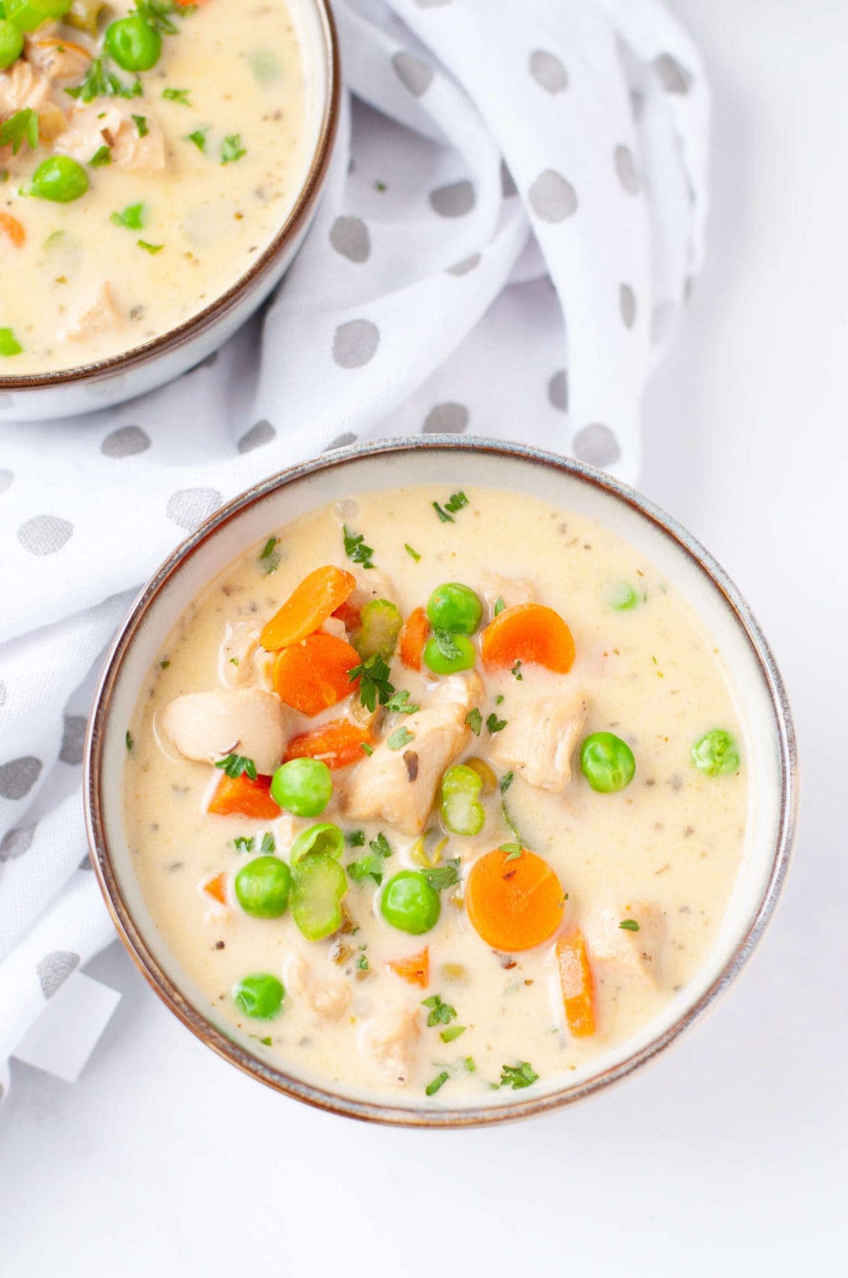 overhead shoot of a bowl of creamy chicken soup topped with carrots, celery, and peas.