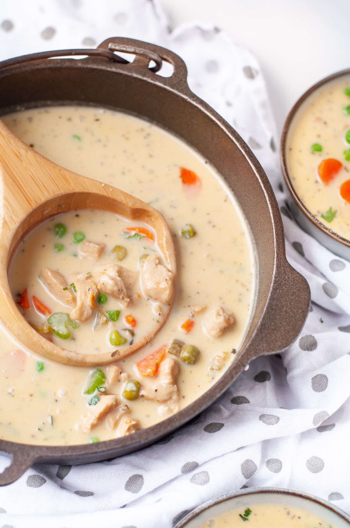 soup crock full of low carb chicken pot pie soup with a wooden ladle and bowls of soup around it