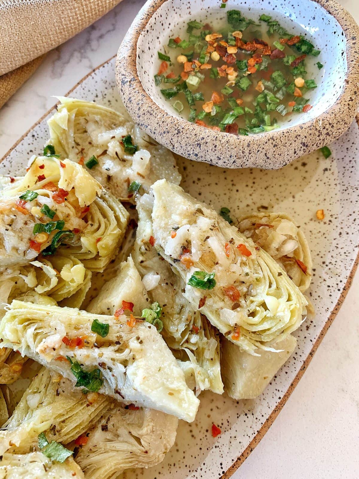 Overhead shot of marinated artichoke heart on a speckled ceramic plate