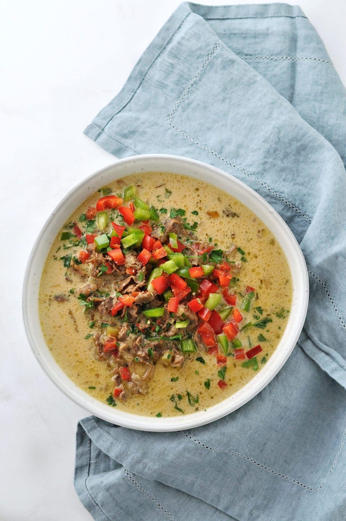 Overhead shot of a bowl of soup - Philly Cheesesteak Soup - in a round bowl, garnished with colorful peppers