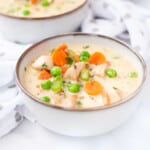 3 bowl of chicken pot pie soup garnished with carrots, peas and celery.