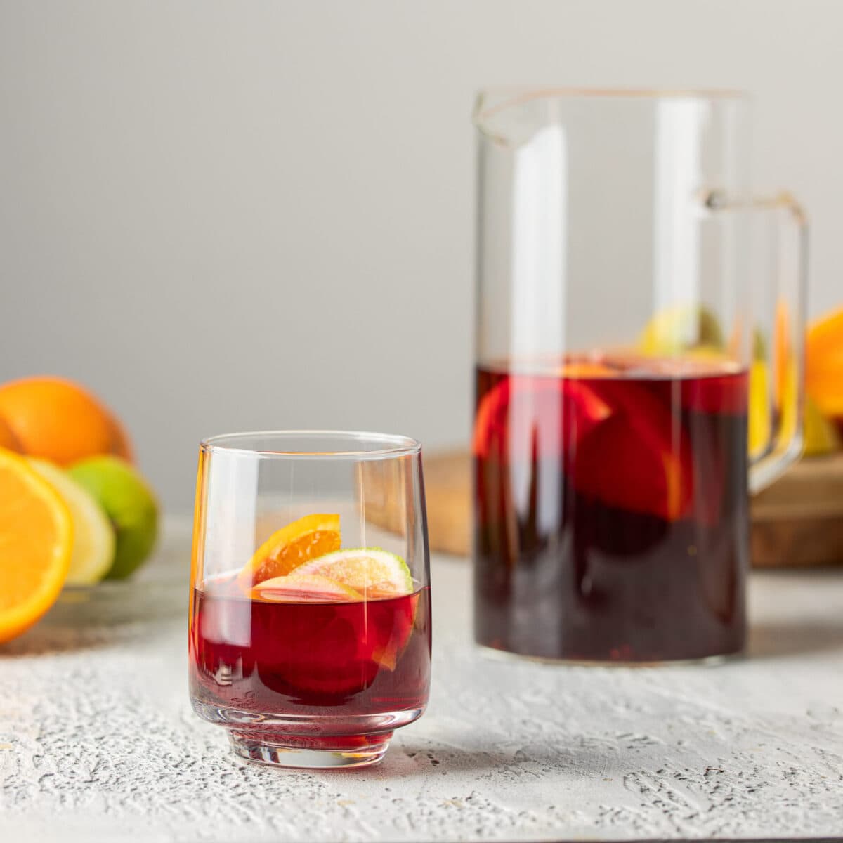 Refreshing pitcher of kombucha in the background with a glass of kombucha with fruit slices in the foreground.