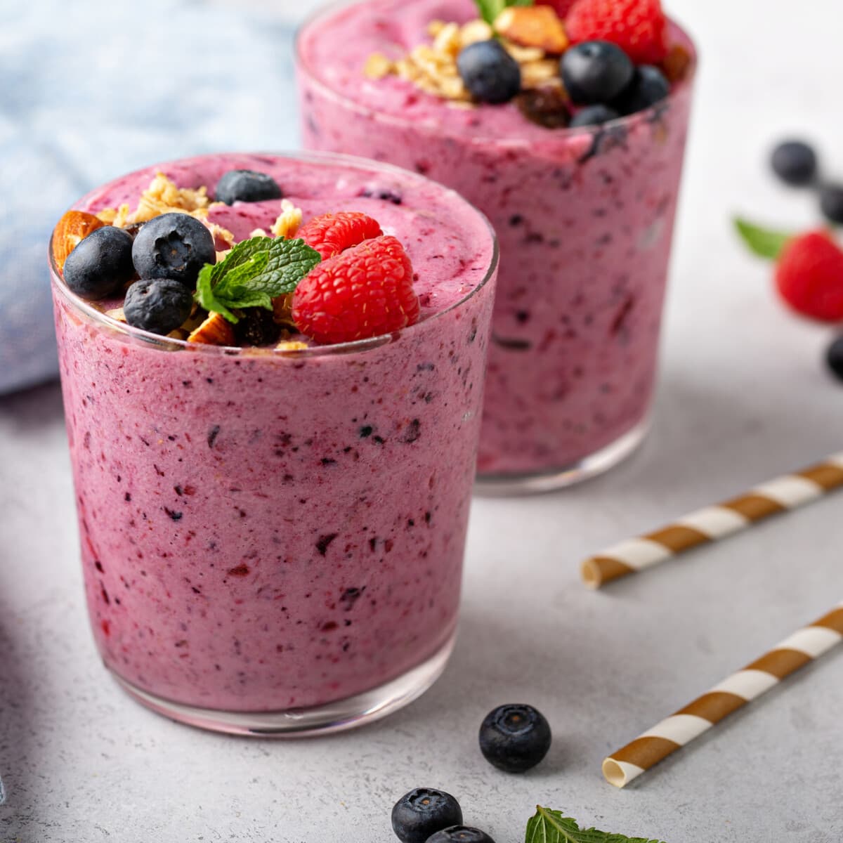 two mixed berry smoothies, topped with crushed nuts, fresh berries, and mint