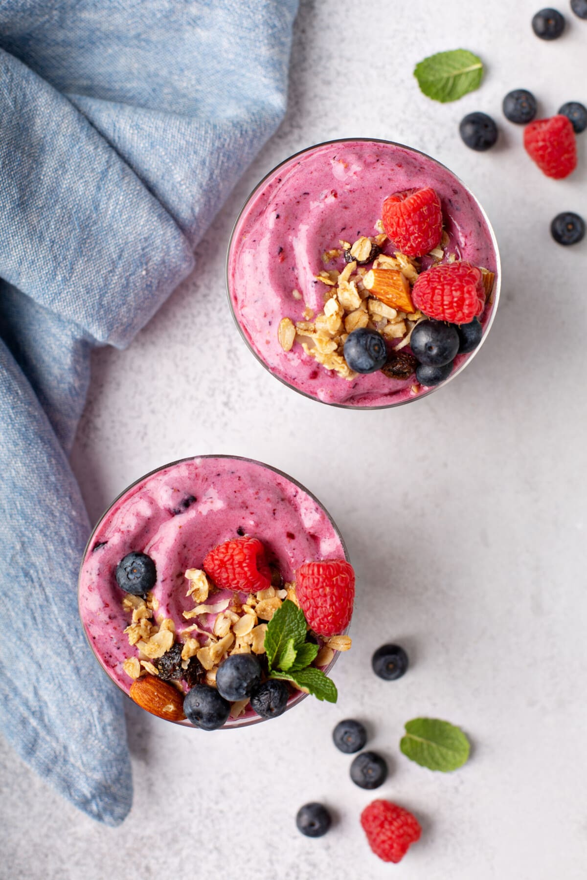 overhead shot of two berry smoothies, topped with crushed nuts, fresh berries, and mint